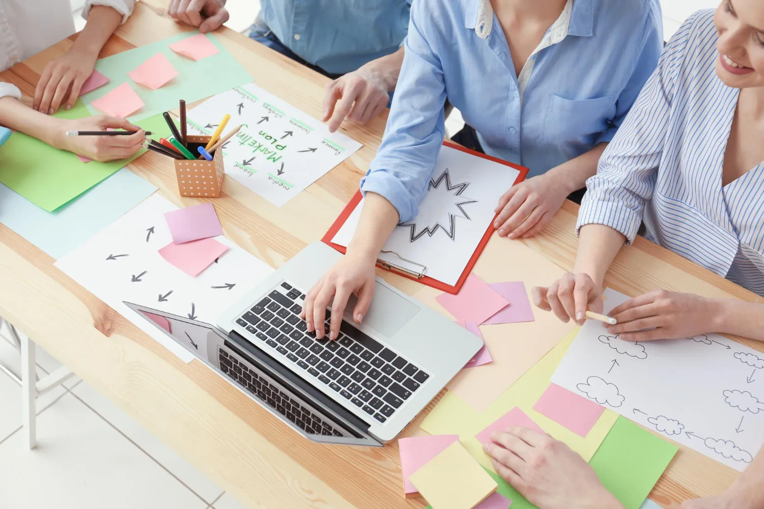 Overhead stock photo of a team brainstorming around a table covered in sticky notes, a hand-drawn marketing plan mind map, and a laptop