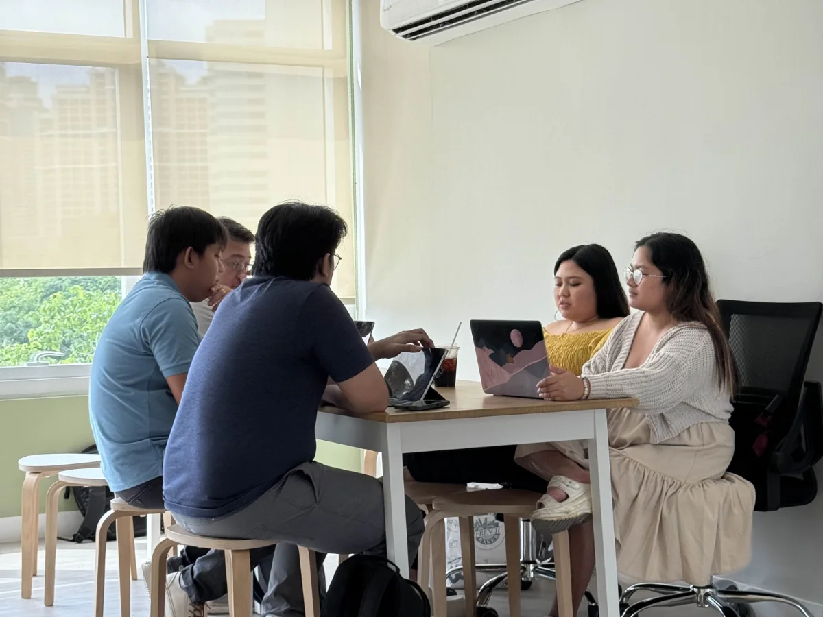 Five of the team working at a table by a window, laptops and tablets between them.